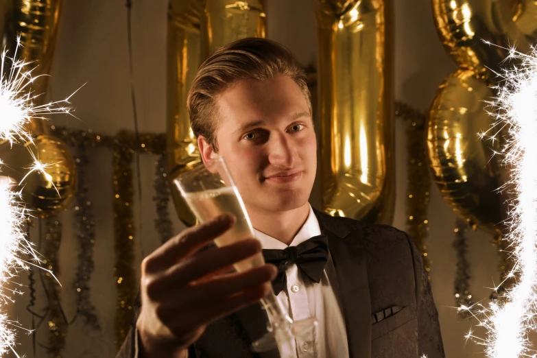 a man wearing a tuxedo holding a small glass with liquid and fireworks