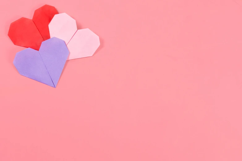 three origami hearts placed on a pink surface