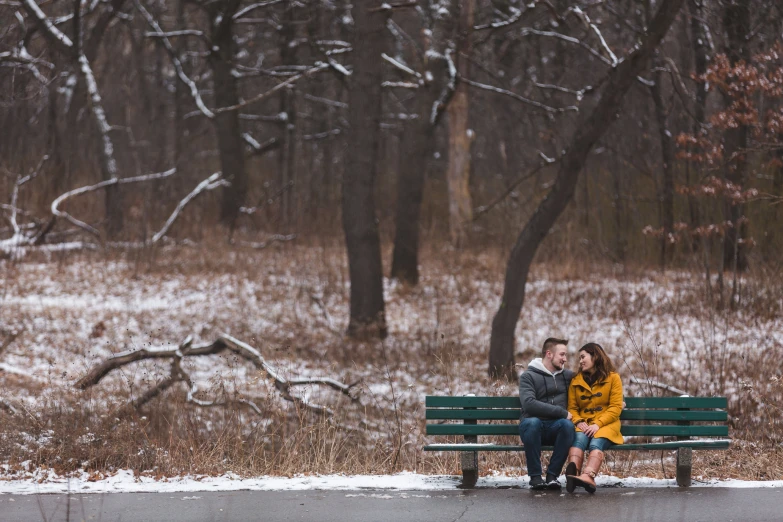 two people sit on a green park bench