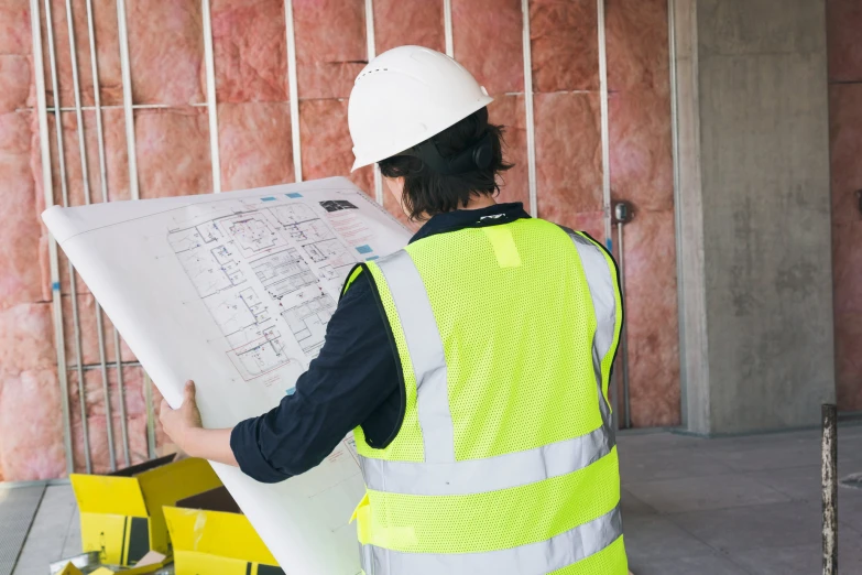 a construction worker holding a white sheet of paper while standing in front of a brick wall