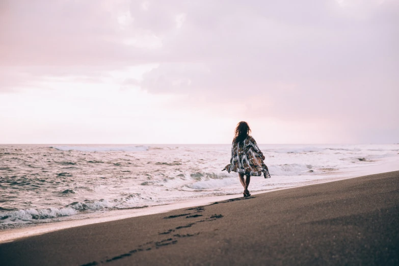a woman walking on the beach, towards the ocean