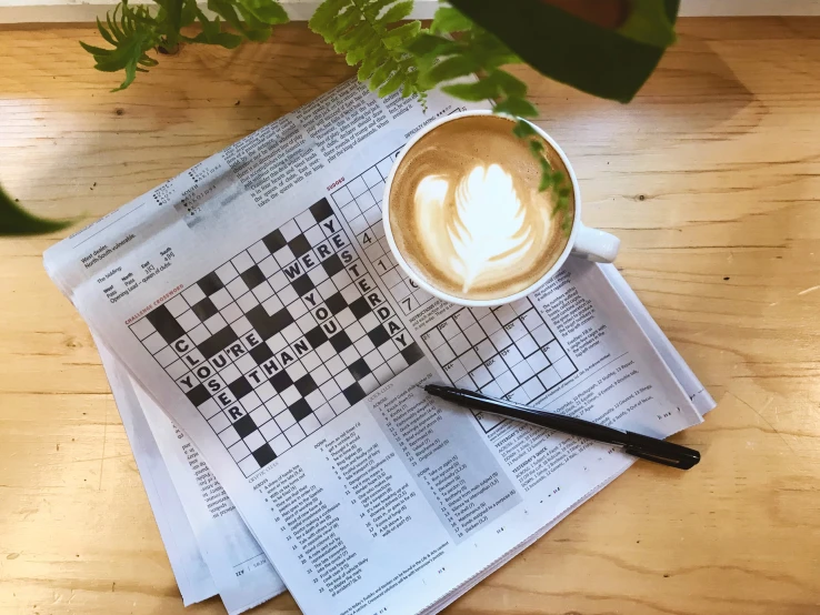 newspaper with crossword and coffee on wooden table