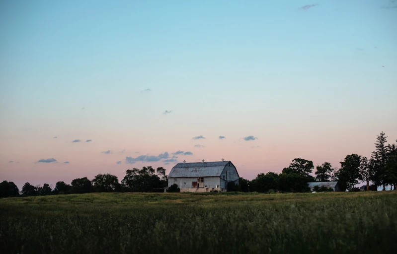 a big field with some grass near a barn