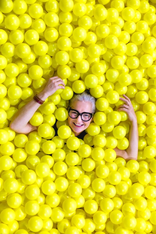 a woman with glasses, in the center of balls, is peering through the middle