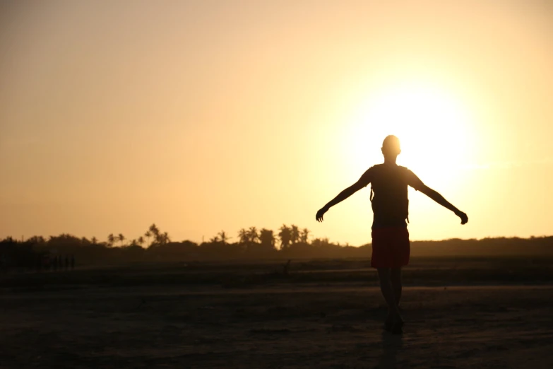 person standing in front of sun holding out his arms