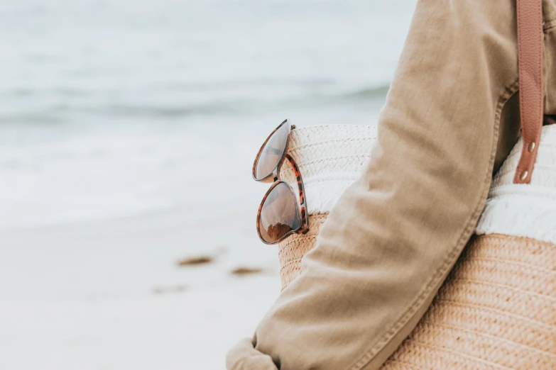 a person's arm, holding a straw bag with sunglasses