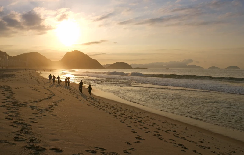 people walking along a sandy beach during a sunset