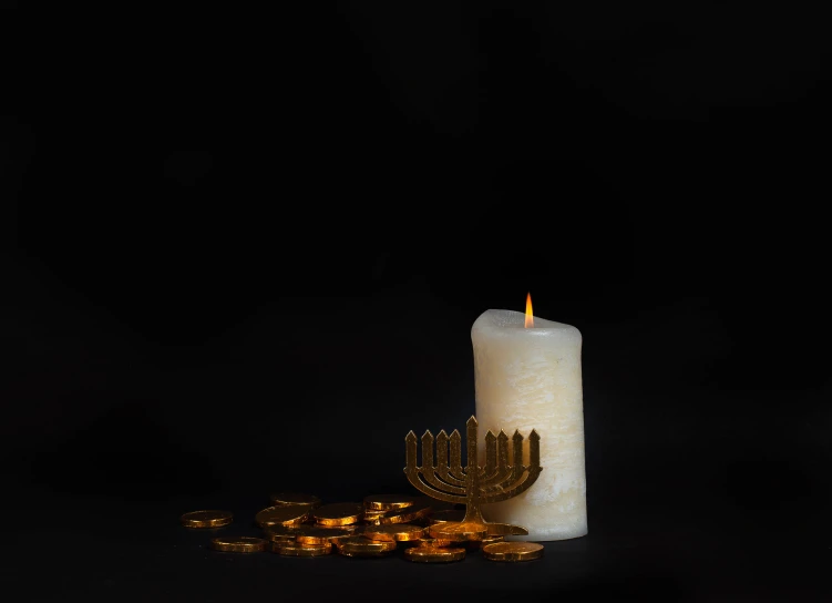 a candle sits in front of a pile of golden coins