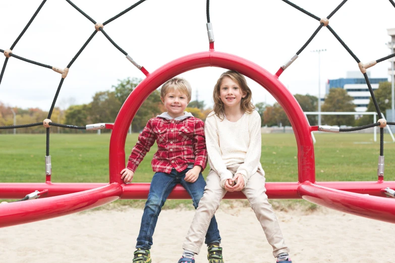 two children sit on the top of a slide at a playground