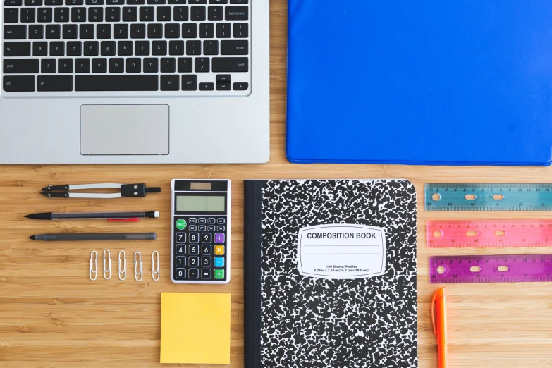 an open notebook next to a calculator, ruler, scissors, and pencils