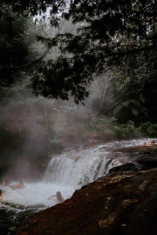 three people sitting in a river watching the water fall