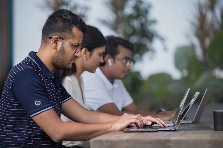 four men sit at a table using laptops