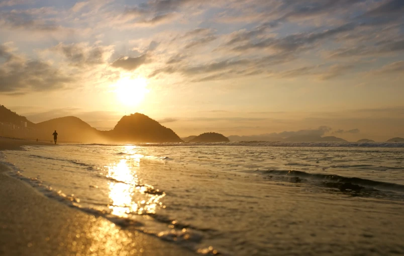 the sun sets over some hills on a beach