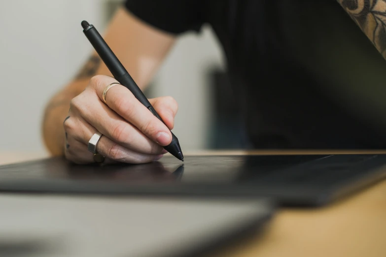 someone sitting at a table with their hands on the surface while holding a pen