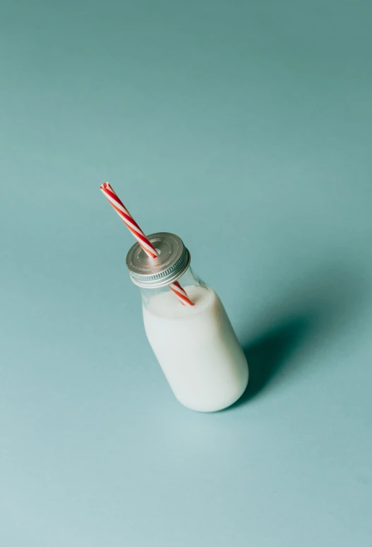 a glass jar with two straws on it next to a bottle of milk