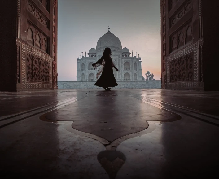 a woman in long black dress walking through an arch