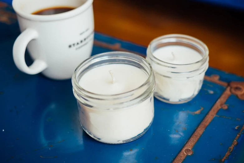 two mason jars filled with white candles sit on a blue table