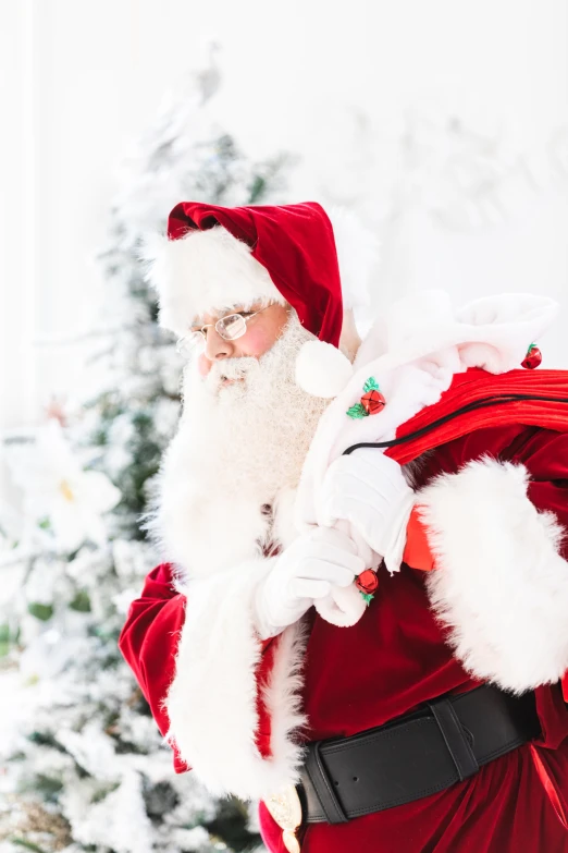 a man in santa claus attire and beard holds a bag in front of a christmas tree