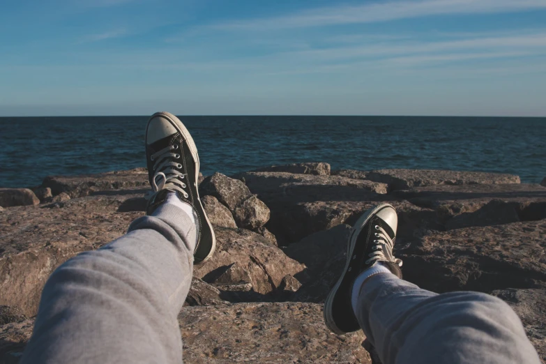 two feet with shoes standing on a rock next to the ocean