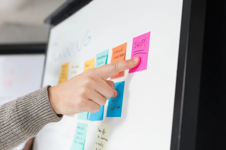 a person points at sticky notes attached to a white board