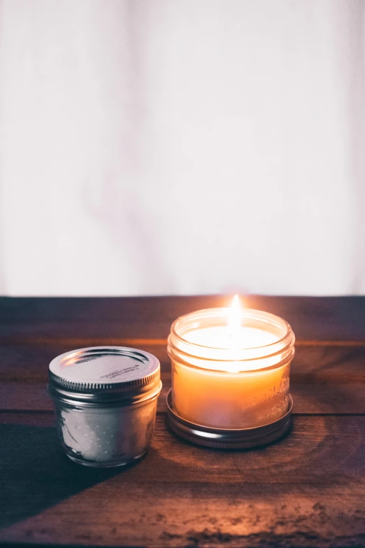 a lit candle sits on a table beside a small jar