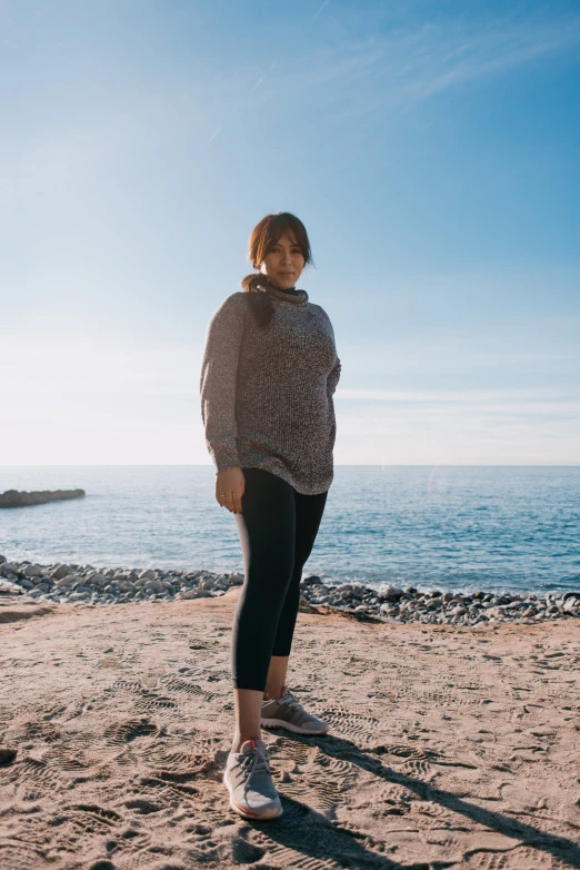 a woman stands on the beach wearing a jacket and leggings