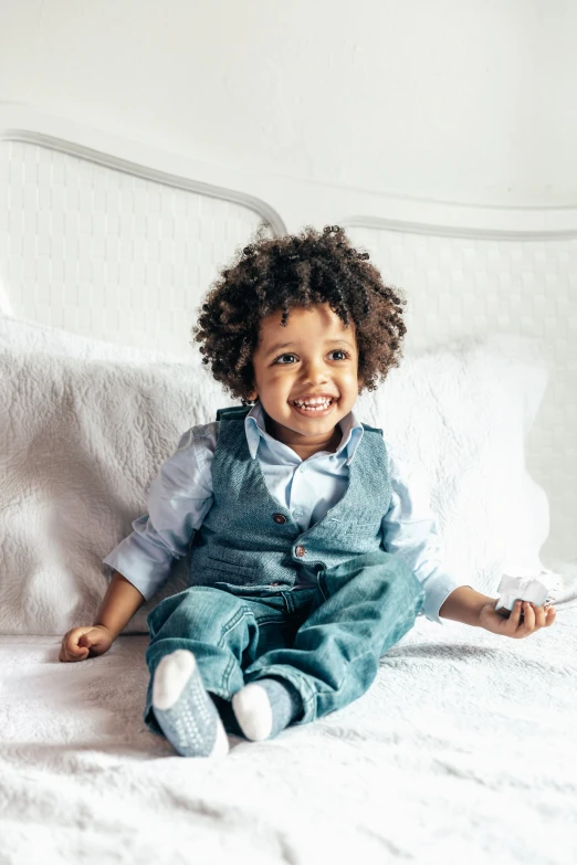 an infant boy smiles and sits on his bed