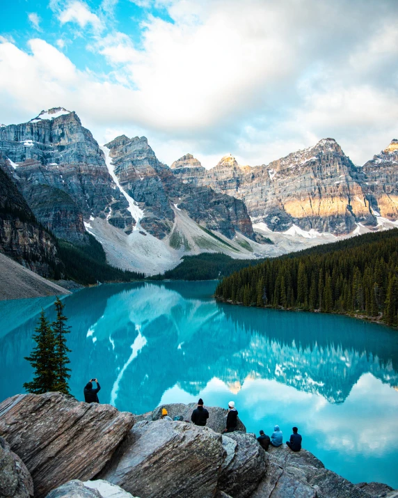 three people on the edge of a large mountain lake