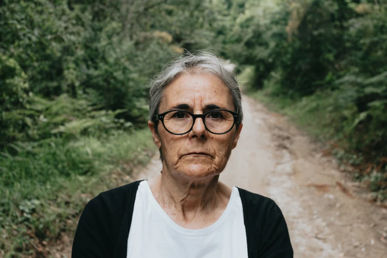 an old woman wearing glasses posing in front of some woods