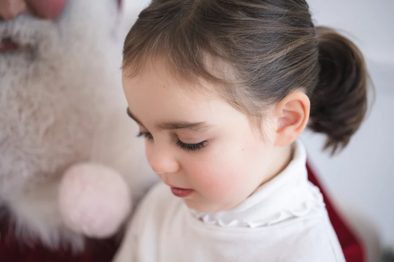 little girl wearing white shirt and bow looking down at santa claus