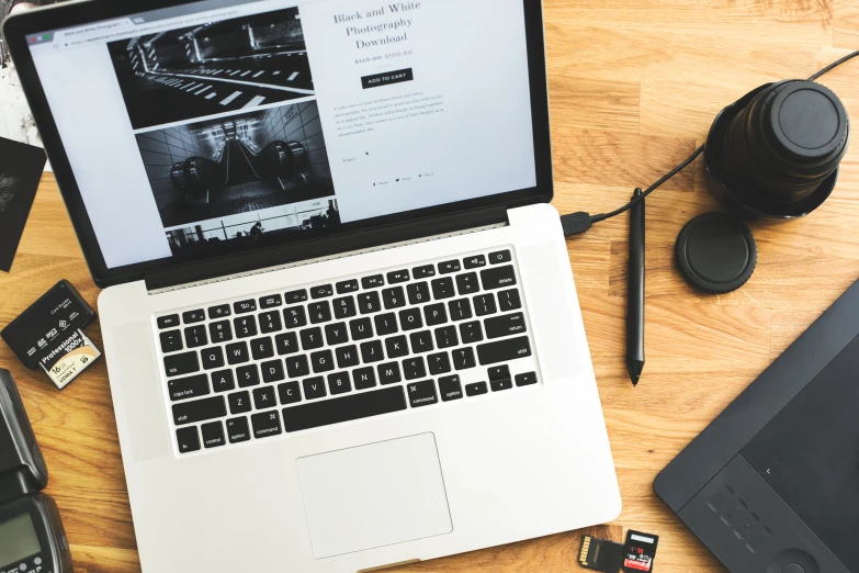 a table with an open laptop, cell phone and camera