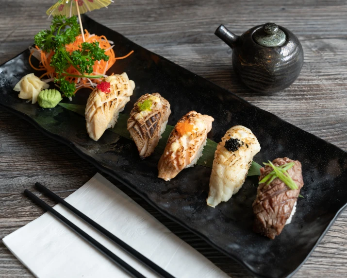 a black plate with sushi on it next to two chopsticks