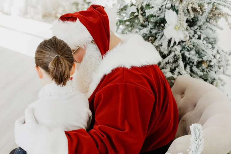 a girl in santa claus costume sitting down and hugging her father