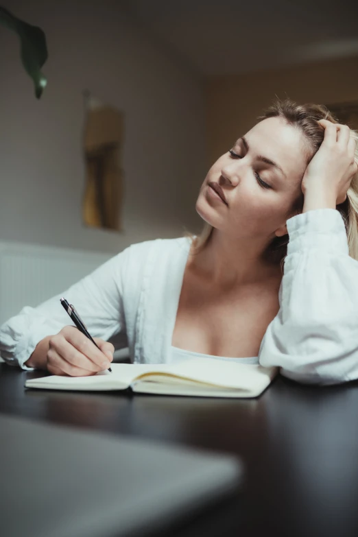 a woman sitting at a table writing on a notebook