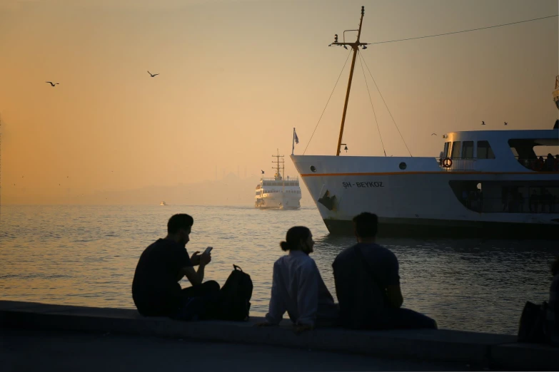 several people sit on a dock, looking out at boats in the ocean