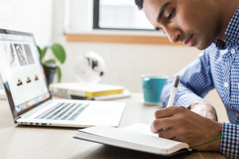 a man with a pen and a notebook in front of a laptop