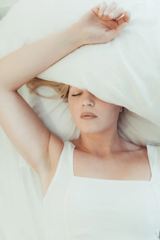 a woman laying in bed holding a pillow above her head