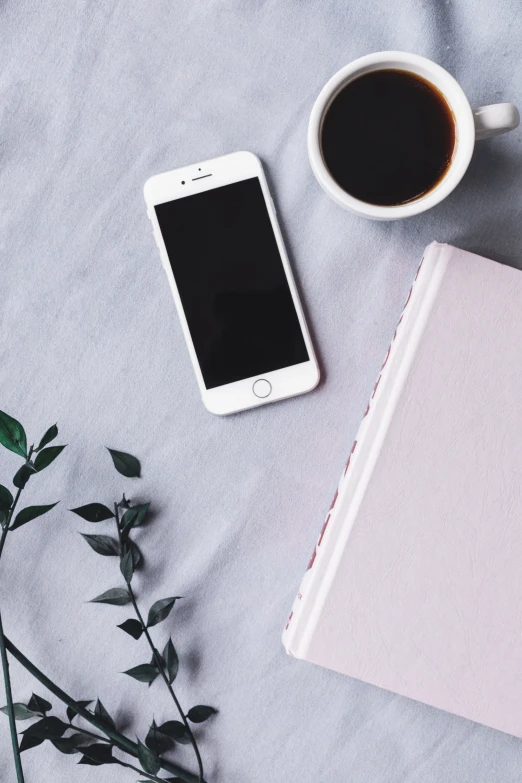 a smart phone next to an open notebook and cup of coffee