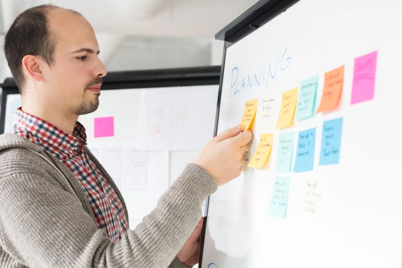 a man is writing on a board with sticky notes