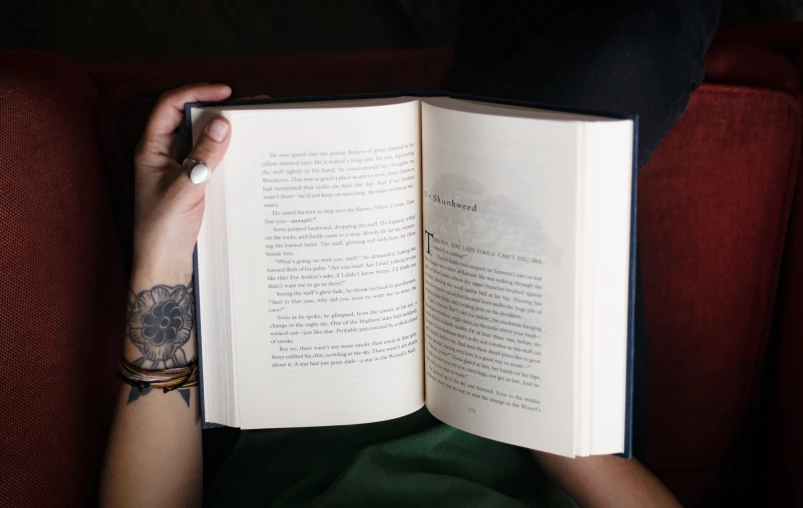 person sitting on the sofa holding a book with an open page in the front