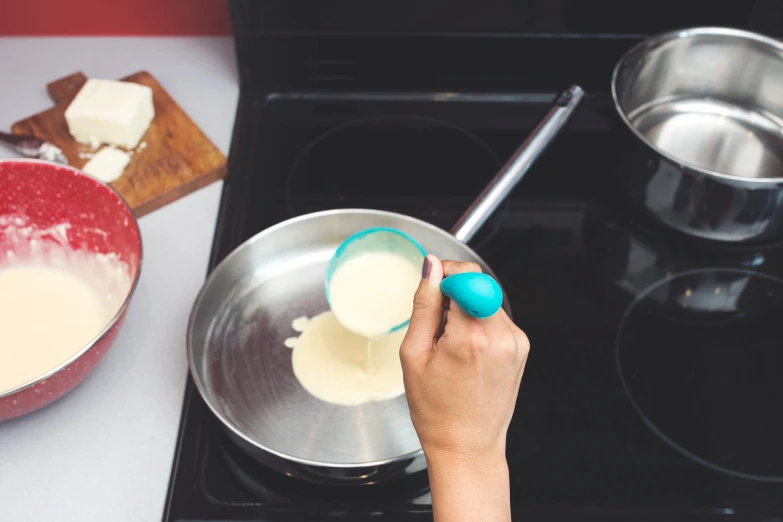 a hand that is holding an egg in a bowl on top of the stove