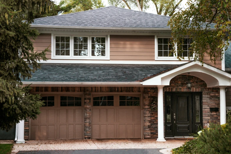 a brown brick house with two garages and trees