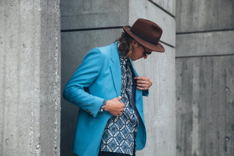 a man in a blue coat and hat standing by a building