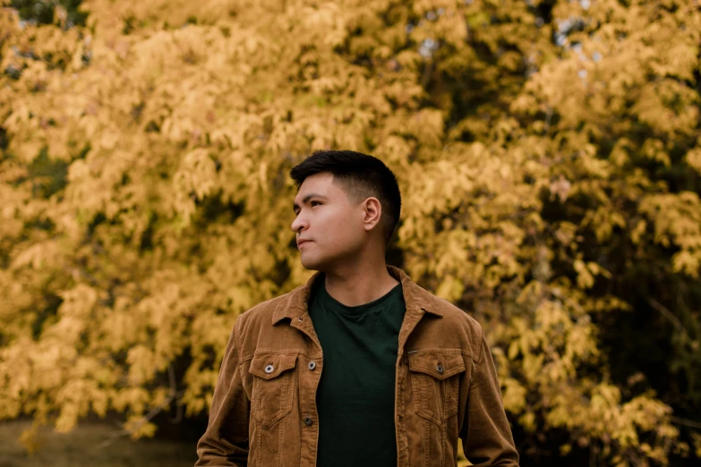 the man stands in front of a tree with bright orange leaves