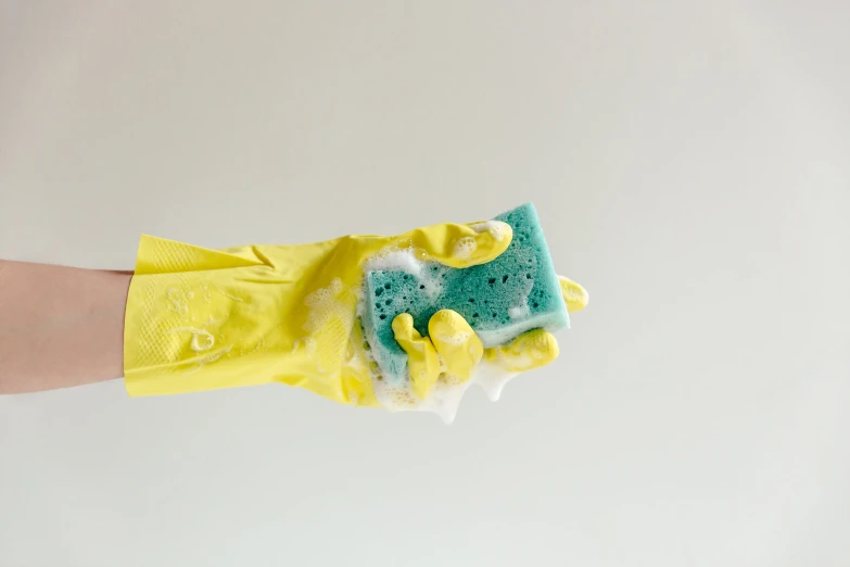 a hand wearing yellow gloves is holding a blue sponge