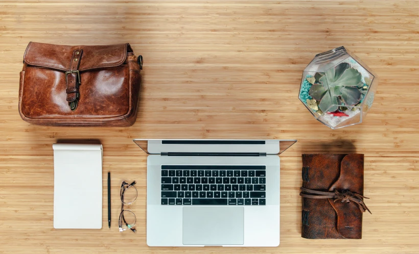 a white laptop sitting on top of a wooden table next to a purse and other items