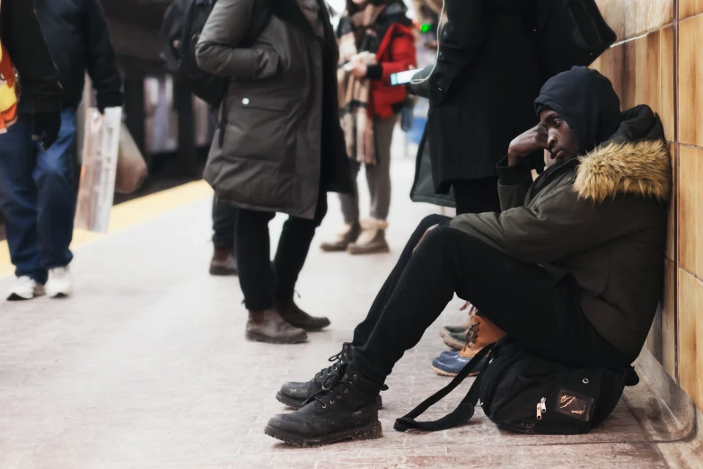 a homeless man sitting on the side of a train platform