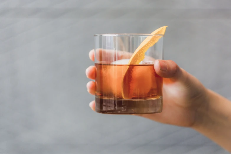 a hand holding a glass filled with ice and a orange wedge