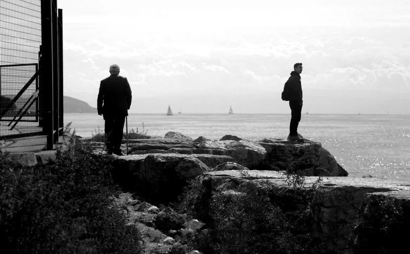 two men are standing by the ocean watching ships