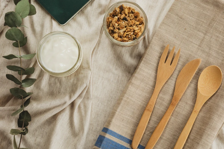 a bowl of granola with two wooden forks, a glass of milk and two spoons